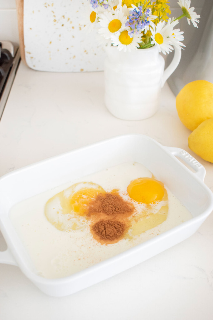ingredients for meyer lemon french toast in a white shallow baking dish on the kitchen counter.