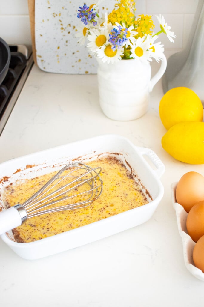 meyer lemon french toast mixture mixed up with a whisk in a white shallow baking dish on the kitchen counter.