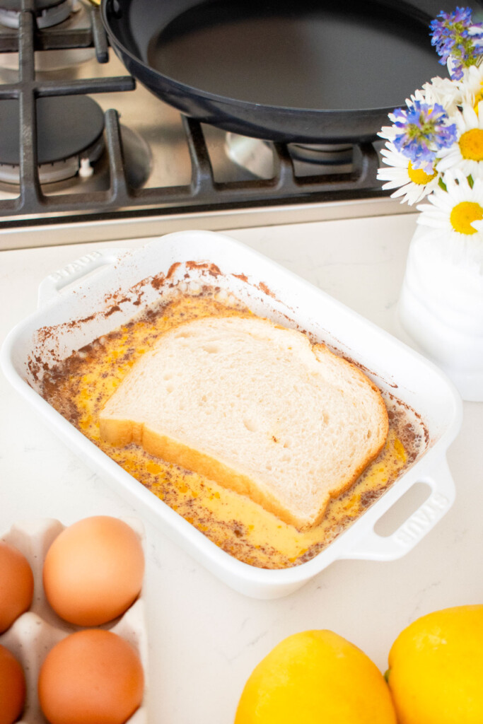 bread soaking in meyer lemon french toast mixture in a white baking dish on the kitchen counter.