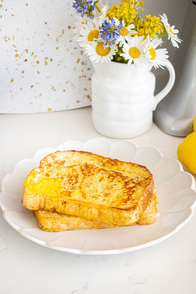 meyer lemon french toast slices on a white ruffle plate on a white counter with fresh flowers.