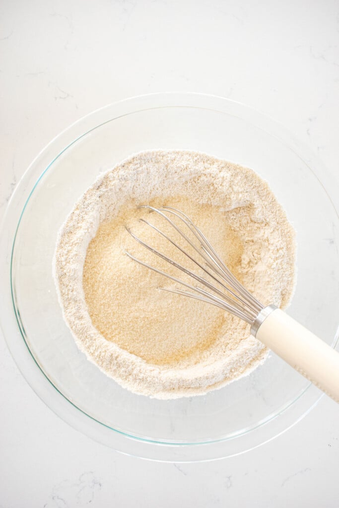 flour and sugar with a whisk in a glass mixing bowl on a marble counter.