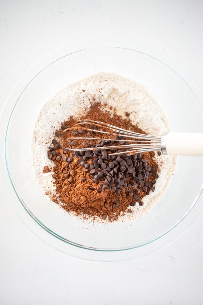 ingredients for olive oil raspberry brownies in a glass mixing bowl with a whisk on a white marble counter.