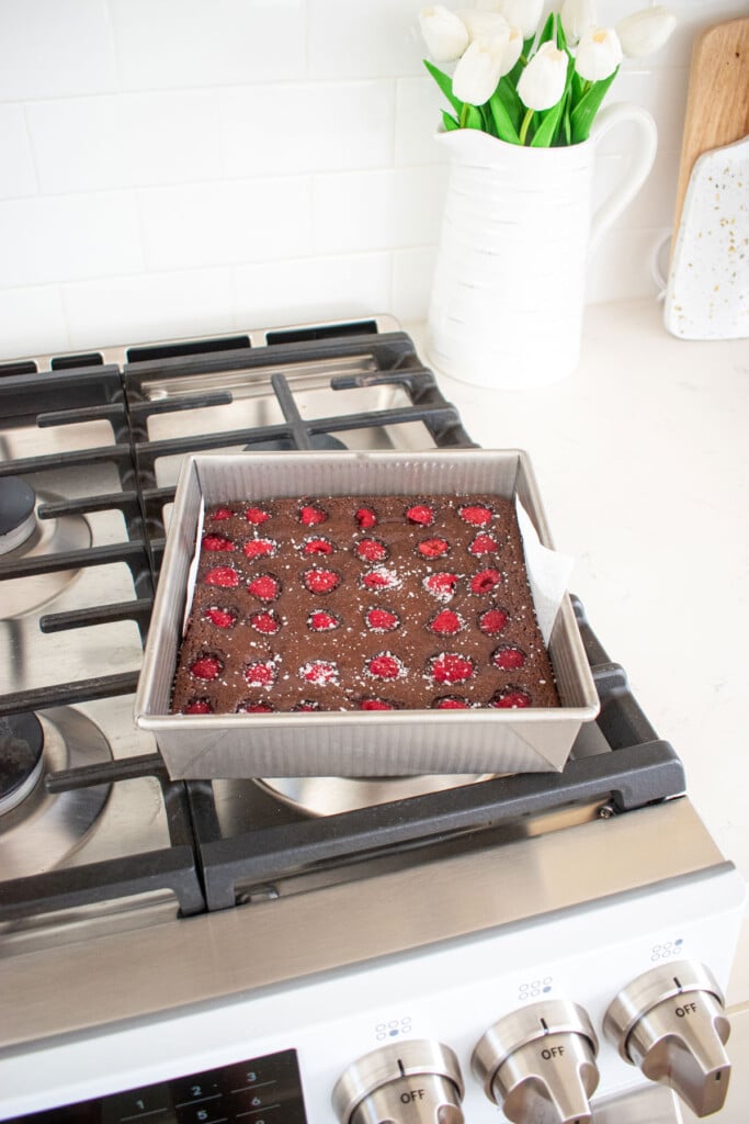 olive oil raspberry brownies in a baking pan cooling on top of the oven.