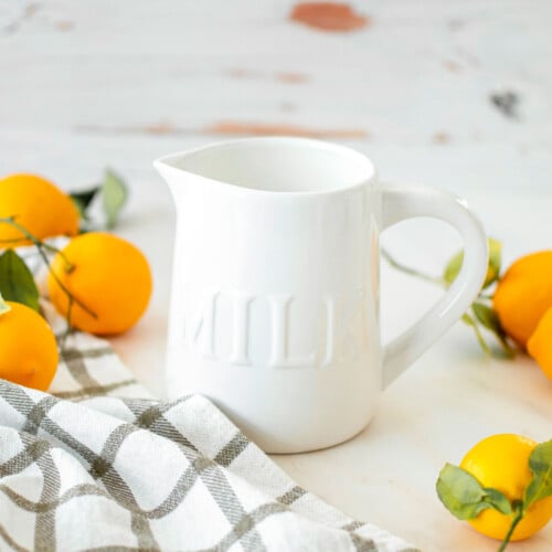 homemade organic buttermilk in a white milk pitcher on a marble counter with lemons all around.