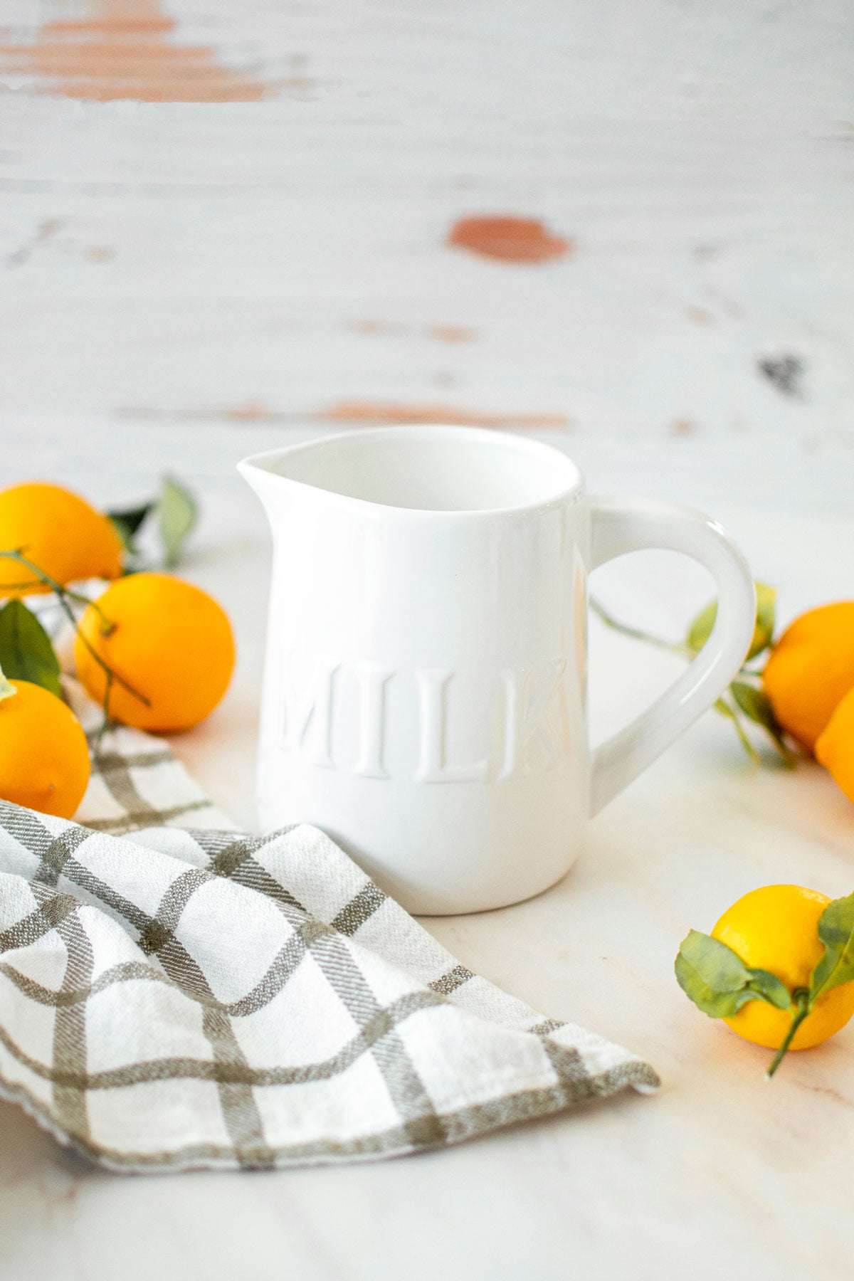 homemade organic buttermilk in a white milk pitcher on a marble counter with lemons all around.