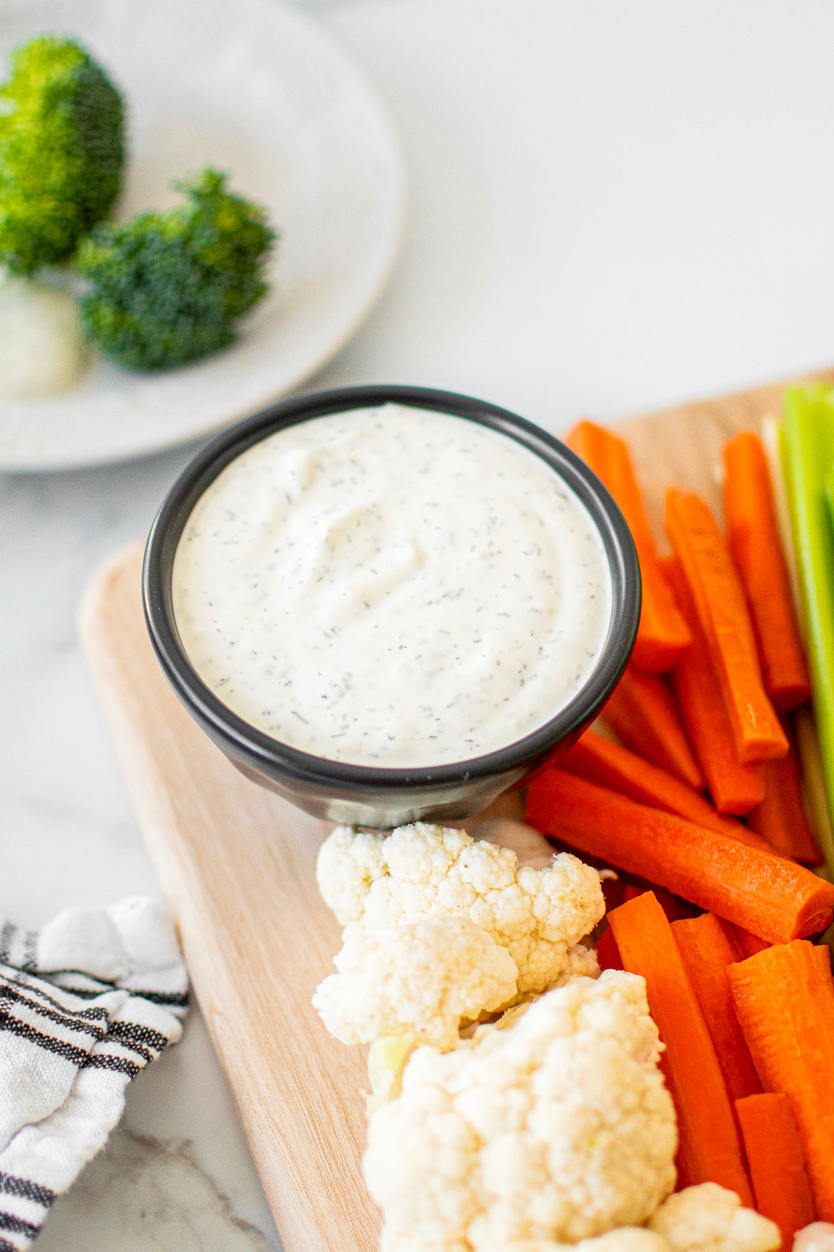 organic dill dip in a bowl on a veggie platter on a white marble counter.