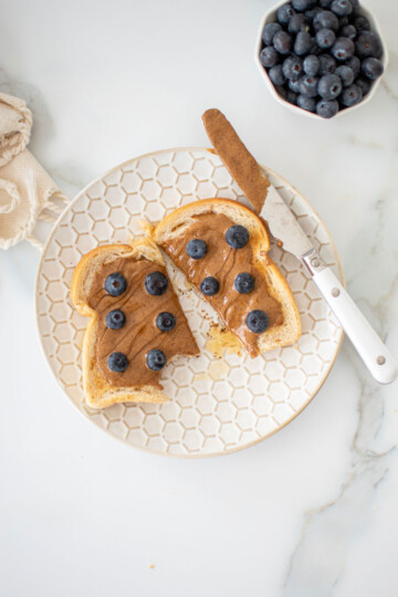 blueberry honey almond butter otast on a plate cut in half with a bite taken out.