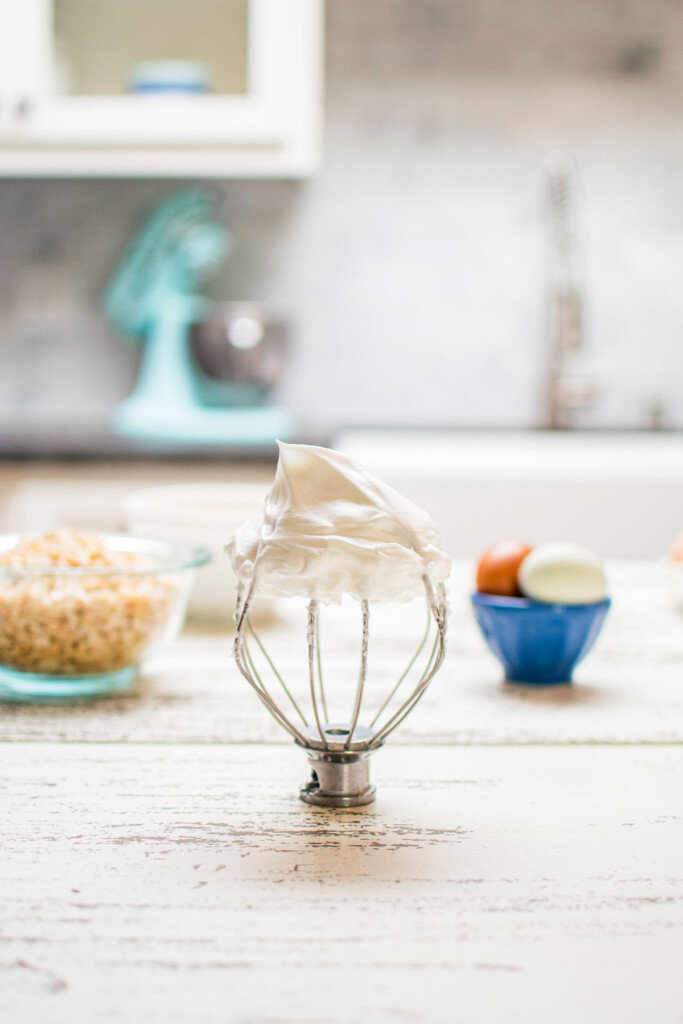 meringue whipped into stiff peaks on a whisk sitting on kitchen counter.