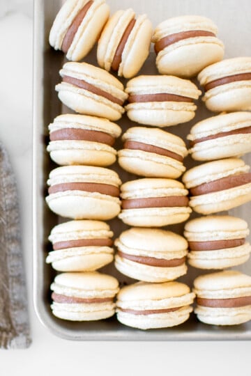 chocolate malt french macarons on a baking sheet on a marble counter.