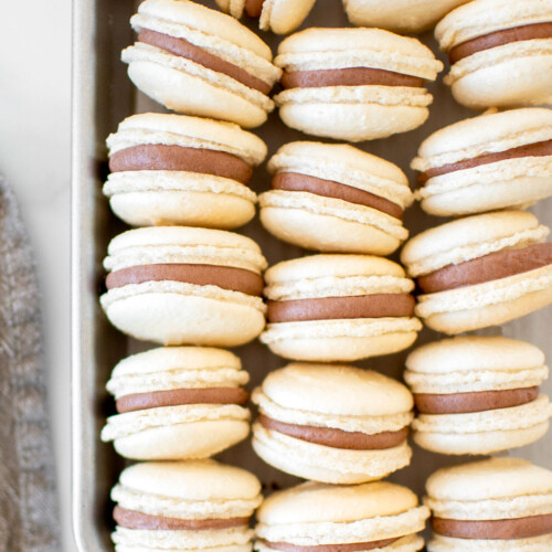chocolate malt french macarons on a baking sheet on a marble counter.