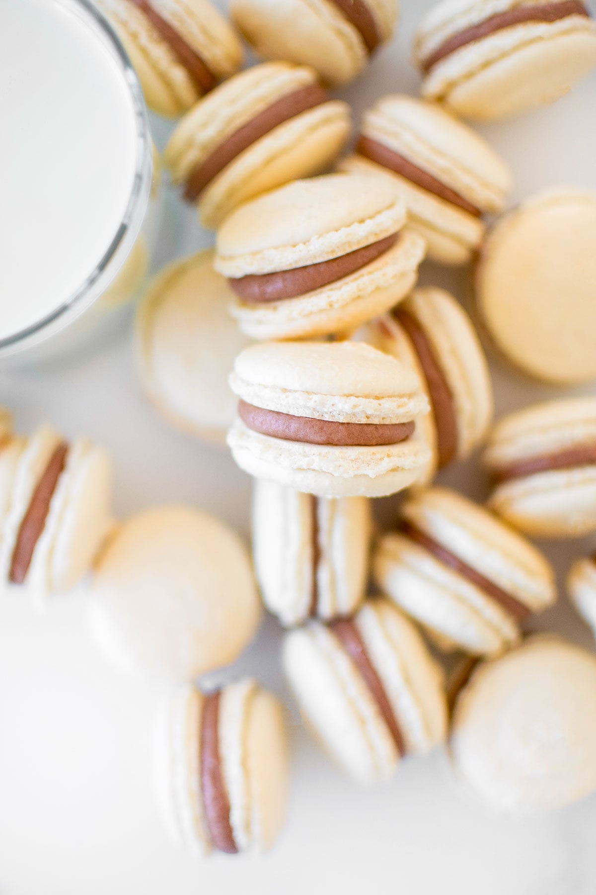 chocolate malt french macarons on a marble counter with a glass of milk.