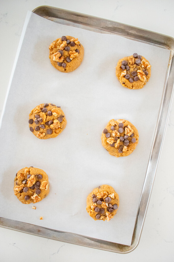 baking sheet with parchment paper and kamut flour chocolate chip cookie dough balls spread out evenly sitting on a marble counter.