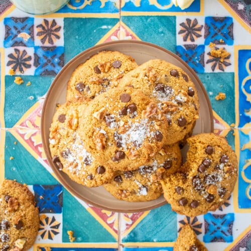 plate of kamut flour chocolate chip cookies on a colorful tile table with a glass of milk and tulips.