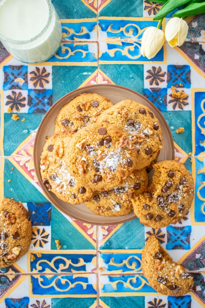 plate of kamut flour chocolate chip cookies on a colorful tile table with a glass of milk and tulips.