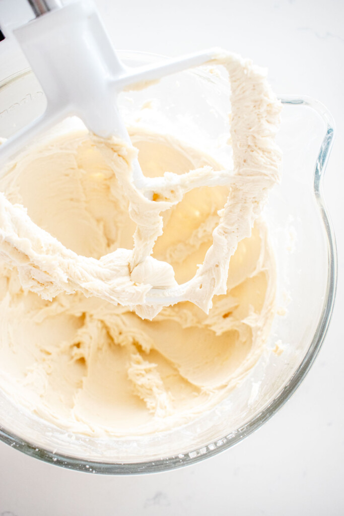 vanilla buttercream frosting in a glass stand mixing bowl on a white marble counter.