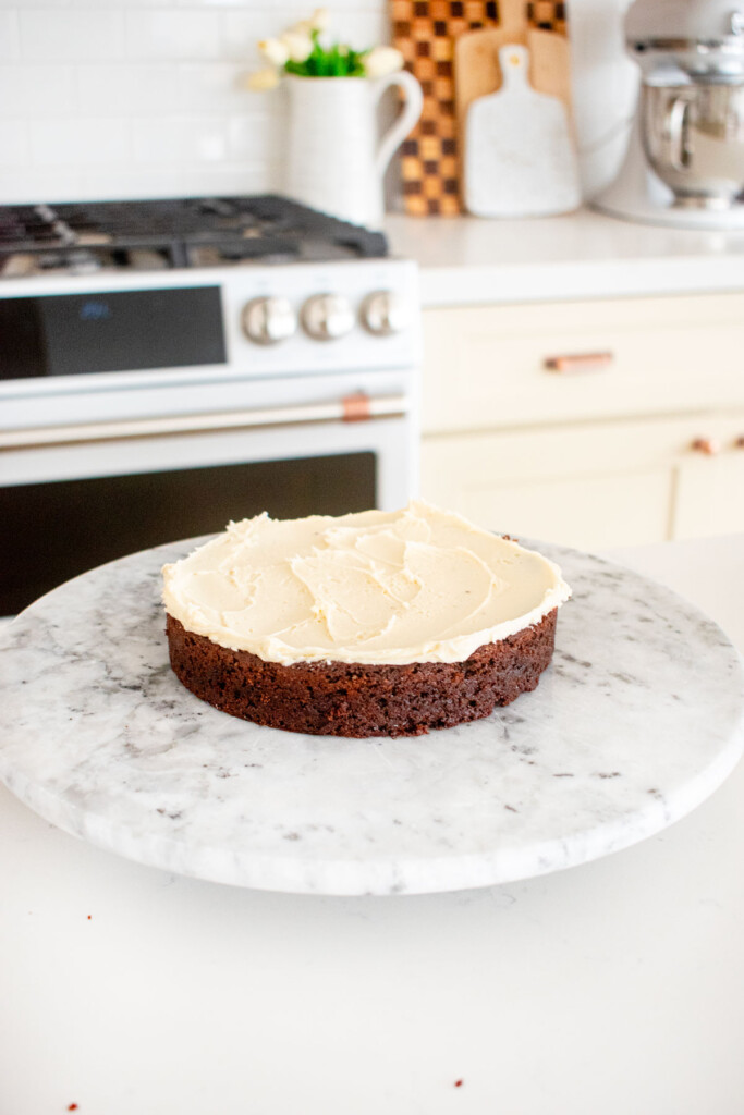 chocolate cake layer on a white marble cake spinner with vanilla frosting spread on top.