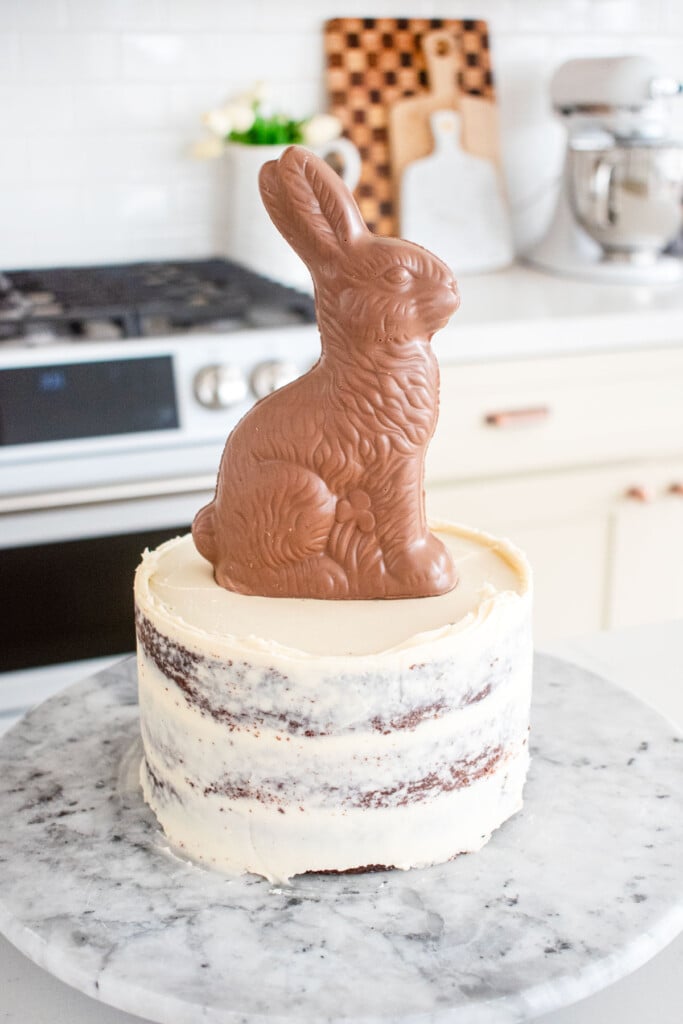 chocolate semi naked cake frosted with vanilla frosting and a chocolate bunny on top on a white marble counter.