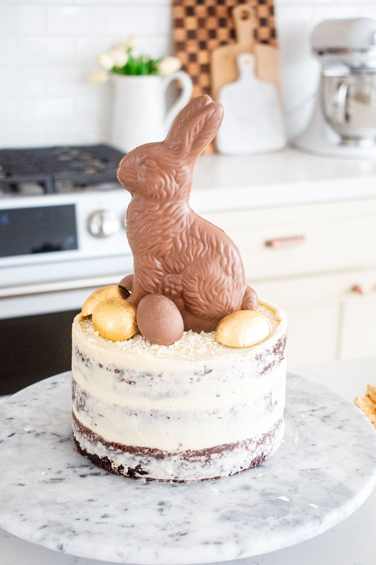 chocolate semi naked cake with a chocolate bunny and eggs on top on a white marble counter.