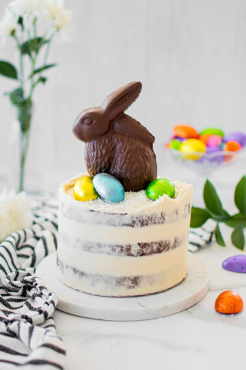 organic chocolate naked cake with a chocolate easter bunny and eggs on top on a white marble counter.