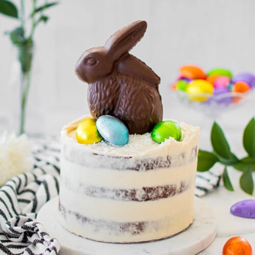 organic chocolate naked cake with a chocolate easter bunny and eggs on top on a white marble counter.