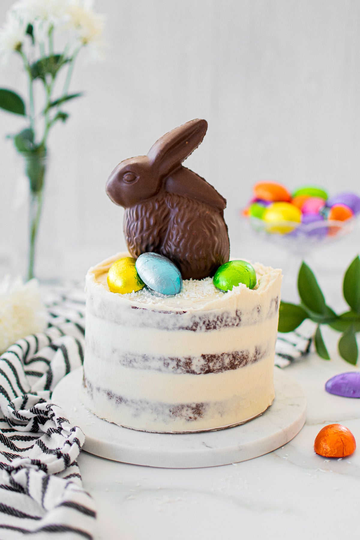 organic chocolate naked cake with a chocolate easter bunny and eggs on top on a white marble counter.
