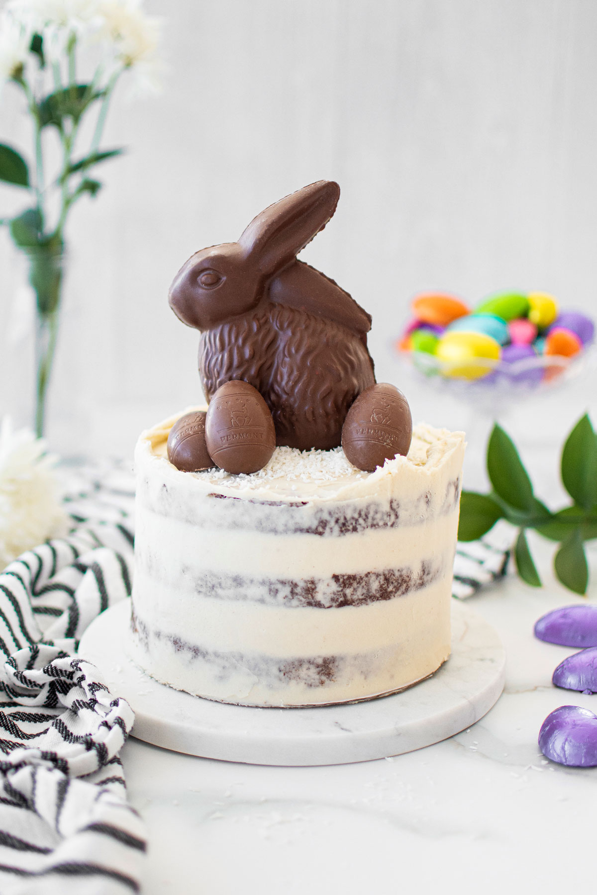 organic chocolate naked cake with a chocolate easter bunny and eggs on top on a white marble counter.