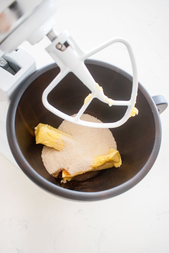 wood mixing bowl with butter and sugar on a white marble counter.