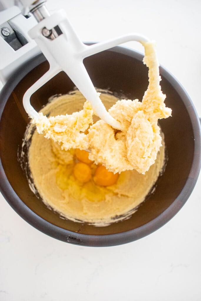 wood mixing bowl with creamed butter and sugar with whole eggs on top on a marble counter.