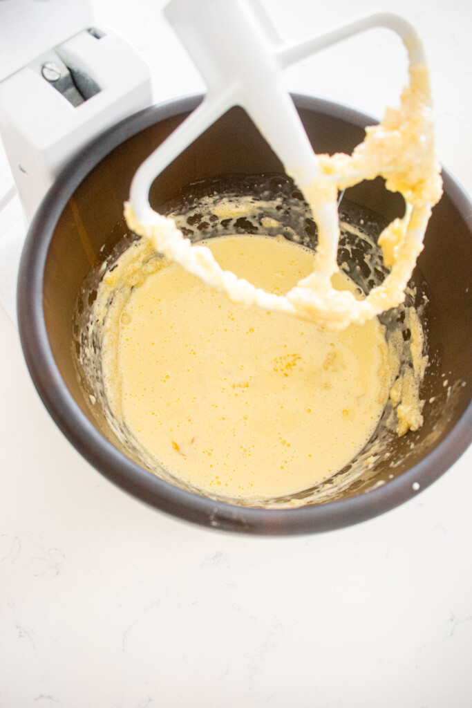 wet ingredients mixed into butter for cake batter in a wood mixing bowl on a white marble counter.