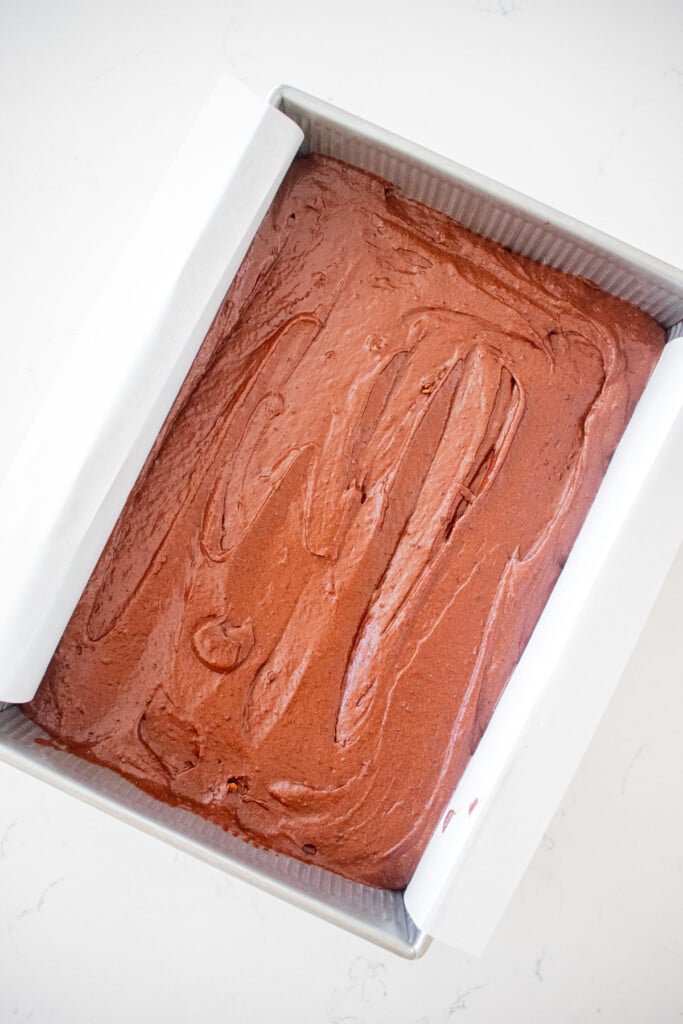 chocolate cake batter in a 9x13-inch baking pan on a white marble counter.