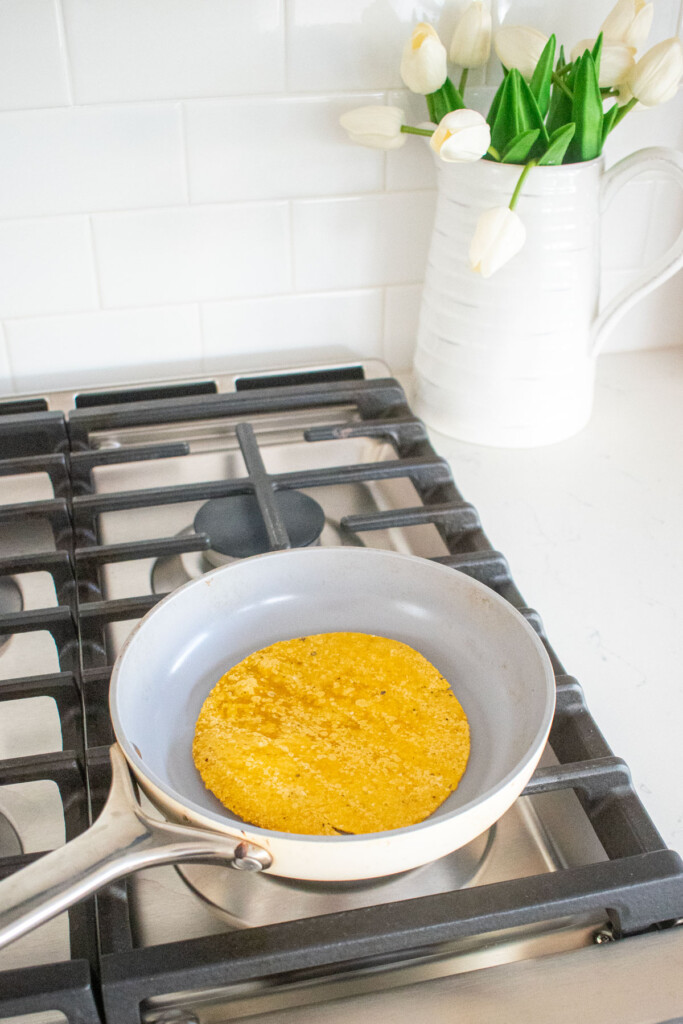 corn tortilla being warmed in a skillet on the stovetop.