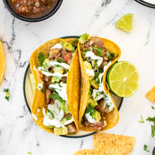 garlic lime chicken street tacos on a plate with chips and salsa on a white marble countertop.