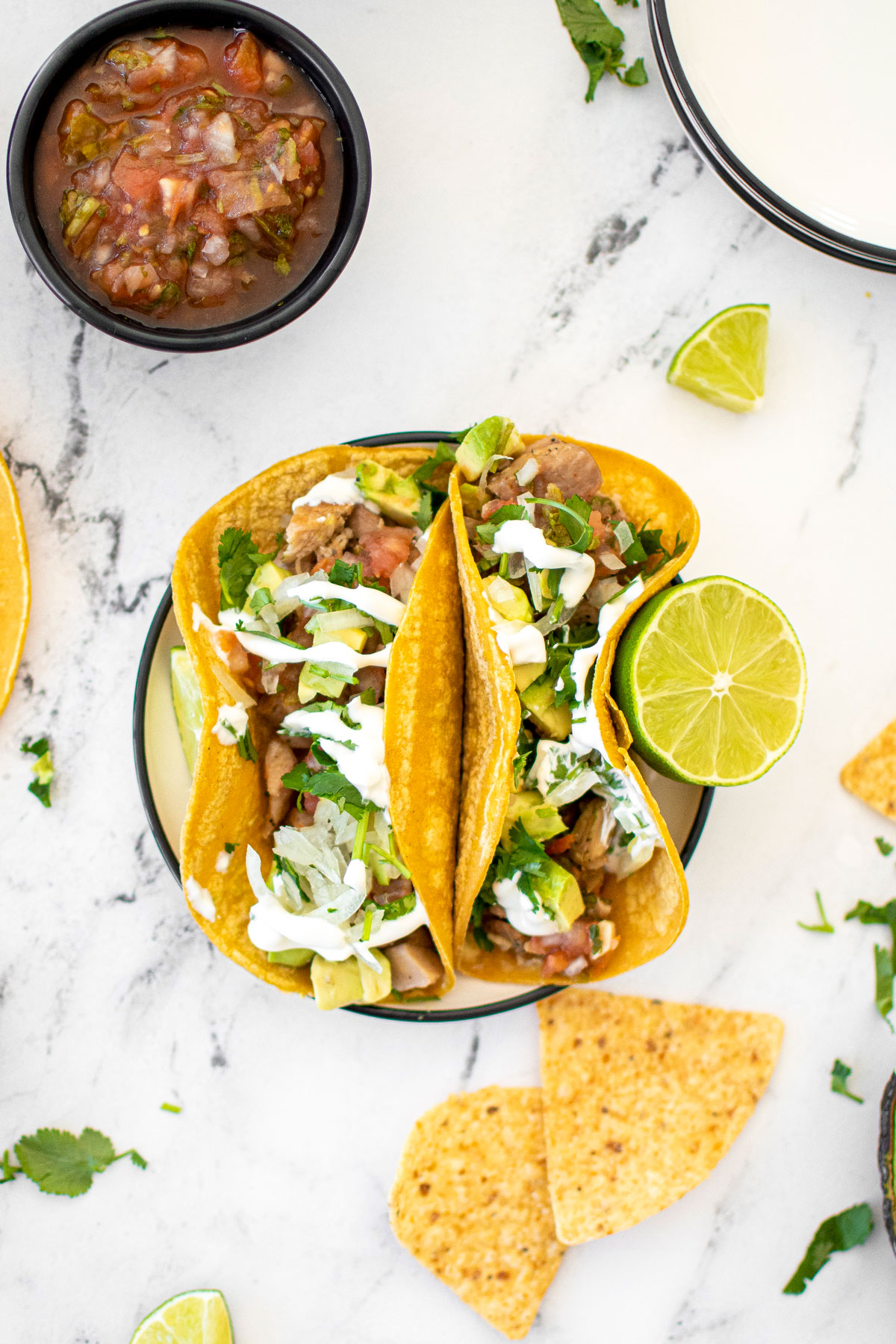 garlic lime chicken street tacos on a plate with chips and salsa on a white marble countertop.