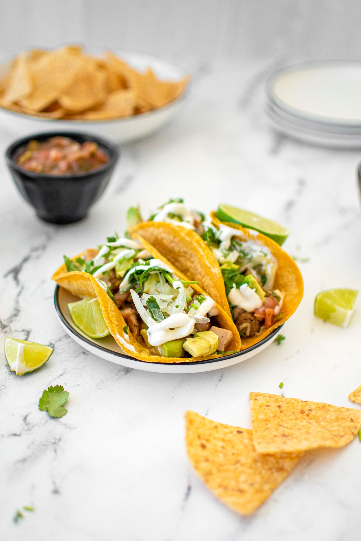 garlic lime chicken street tacos on a plate with chips and salsa on a white marble countertop.