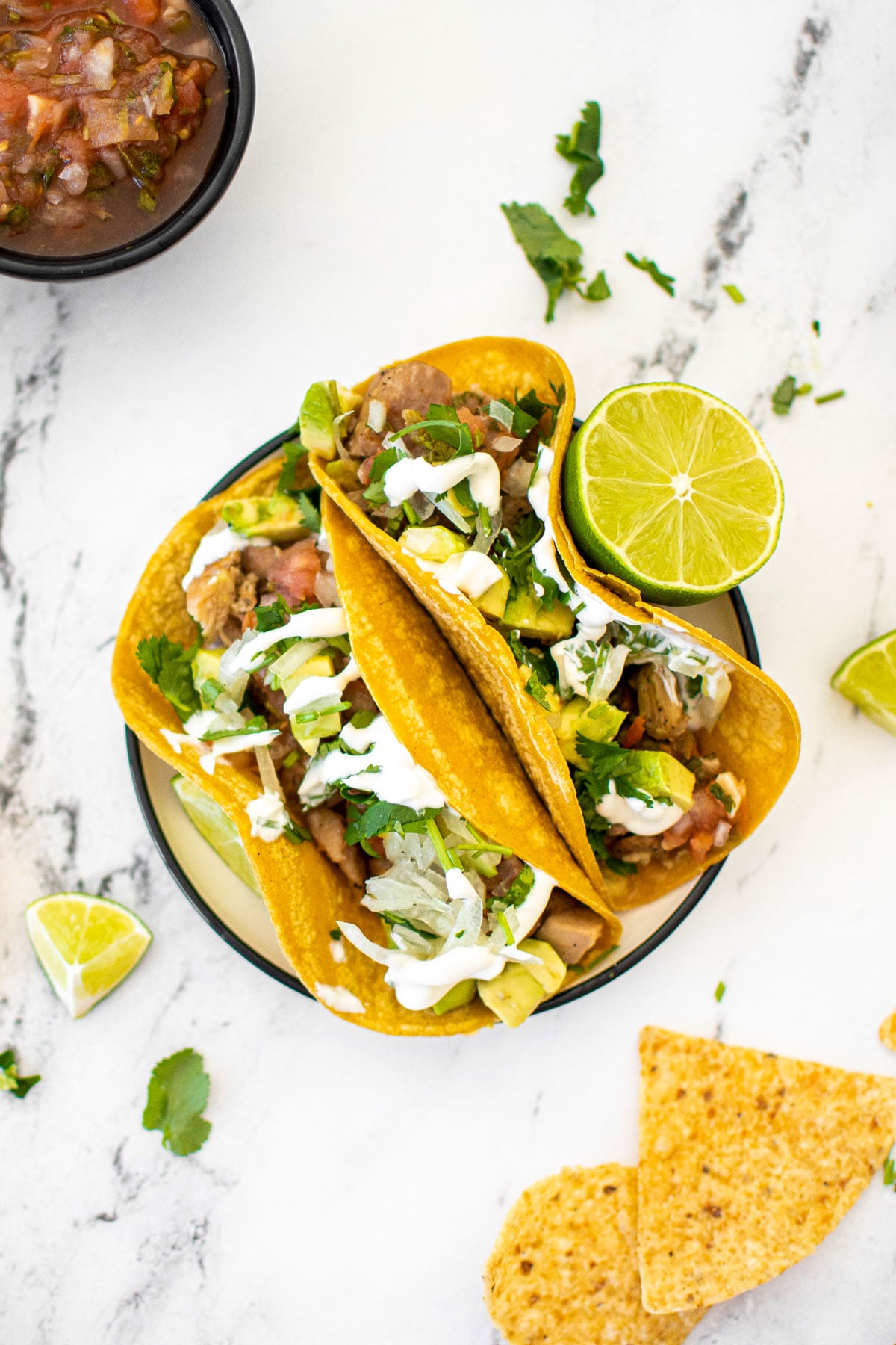 garlic lime chicken street tacos on a plate with chips and salsa on a white marble countertop.