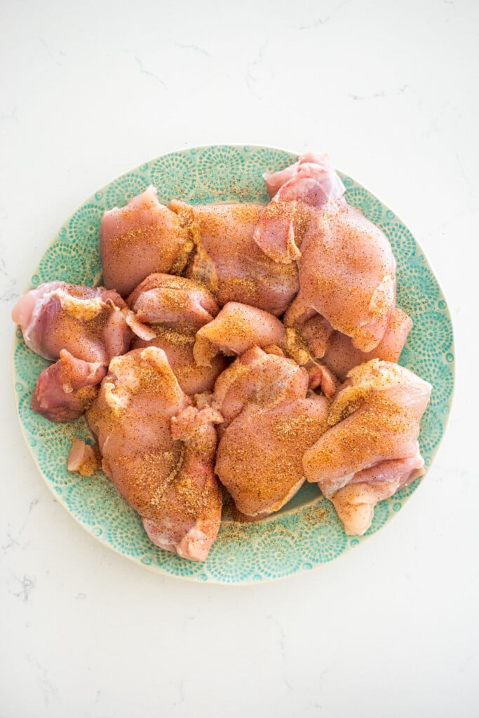 raw boneless skinless chicken thighs on a green plate with taco seasoning on a marble countertop.