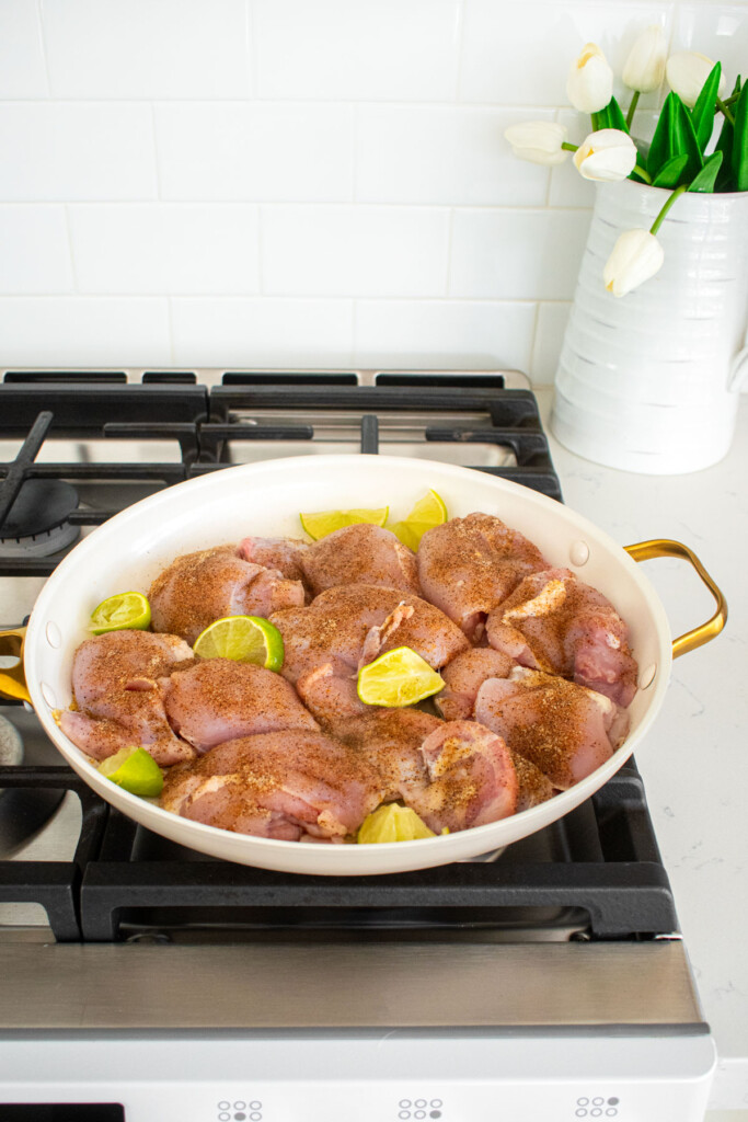 raw chicken thighs with taco seasoning and lime slices in a skillet on the stovetop.