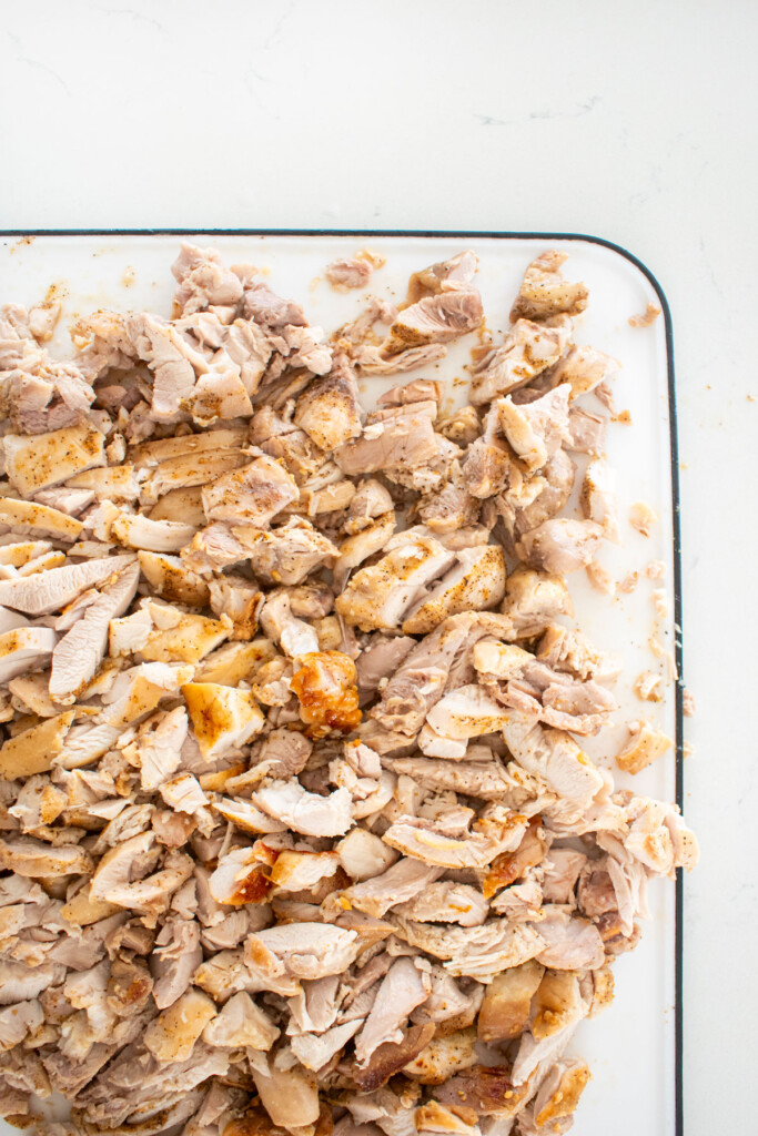 chopped garlic lime chicken on a cutting board on a marble countertop.