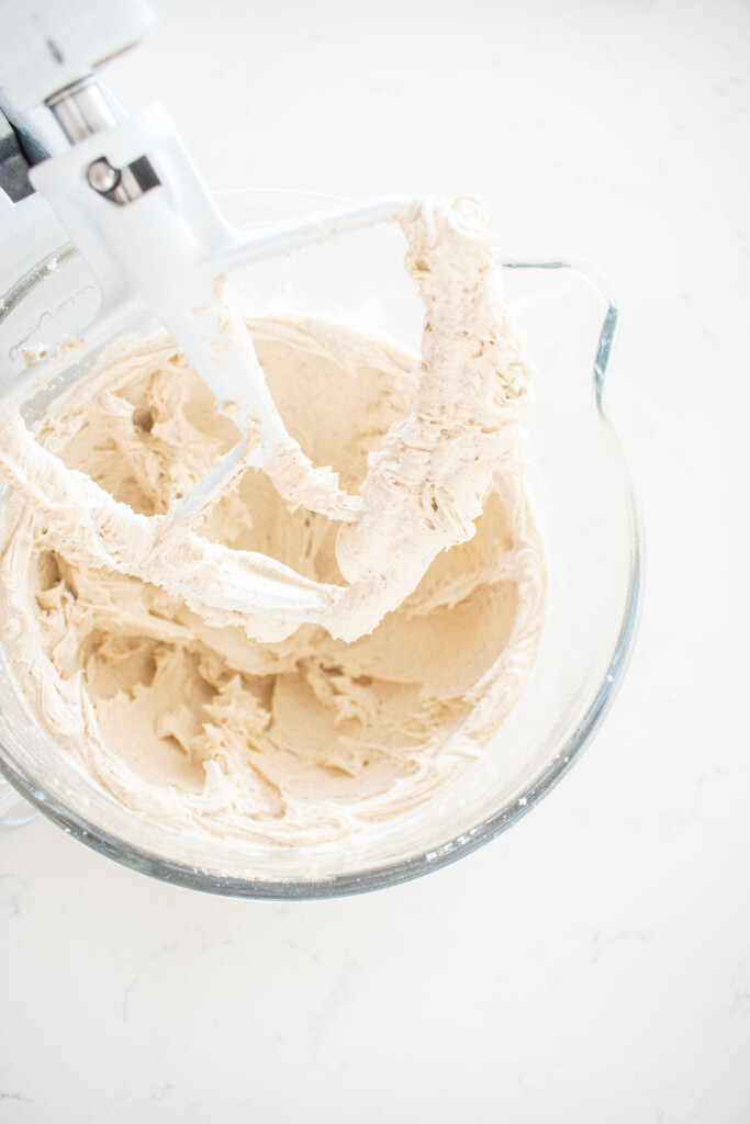 vanilla bean buttercream frosting in a glass stand mixing bowl on a white marble counter.