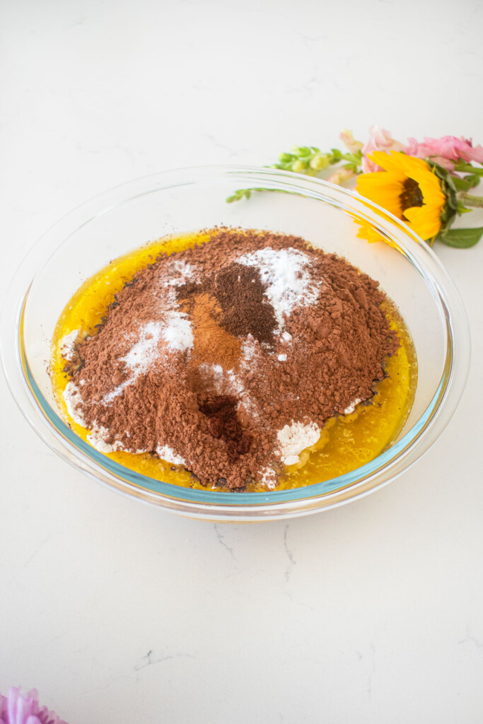 ingredients for vegan sweet potato chocolate cake in a glass mixing bowl on a white marble counter with fresh flowers.