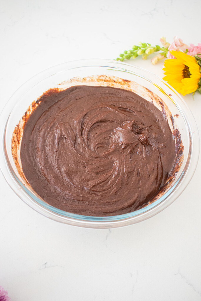 vegan sweet potato chocolate cake batter in a glass stand mixing bowl on a white marble counter with fresh flowers.