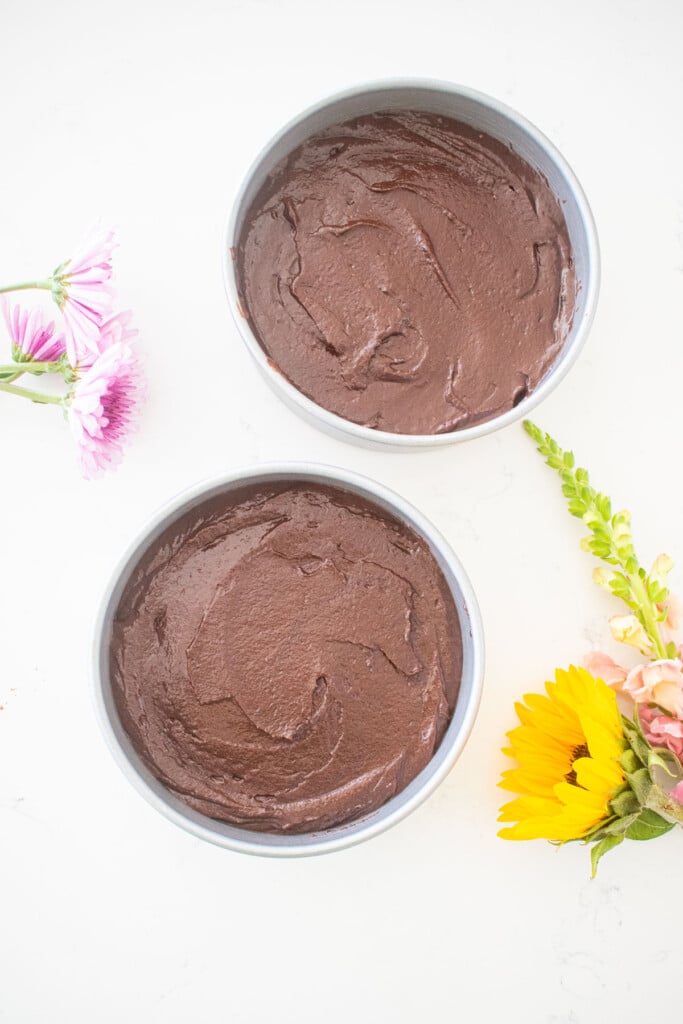 vegan sweet potato chocolate cake batter in two 6-inch cake pans on a white marble counter with fresh flowers.