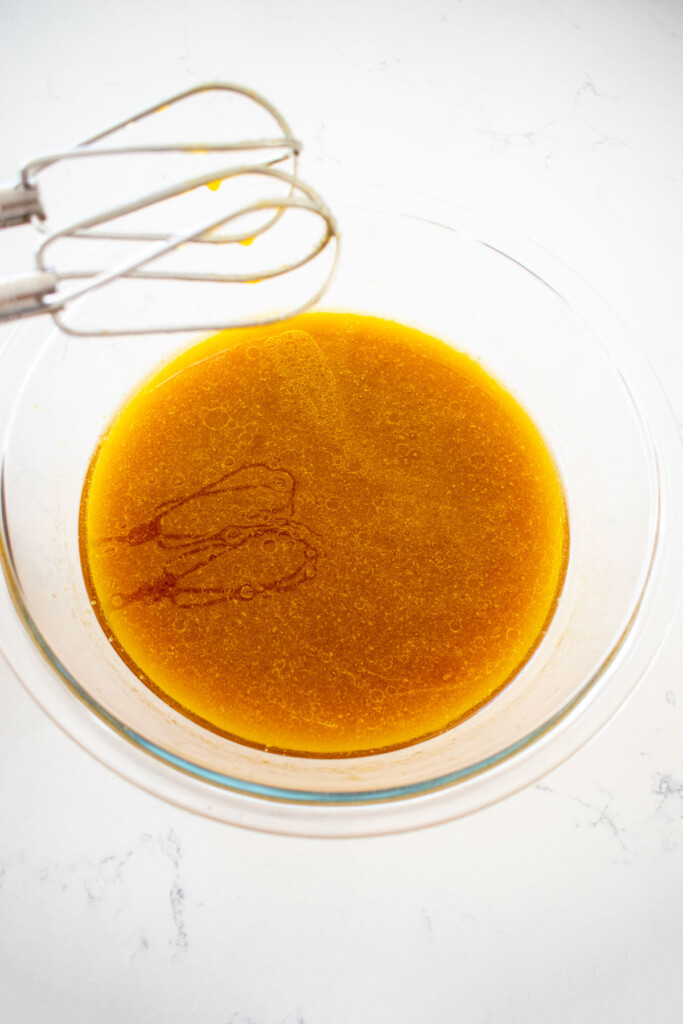 wet ingredients for vegan sweet potato chocolate cake in a glass mixing bowl on a white marble counter.