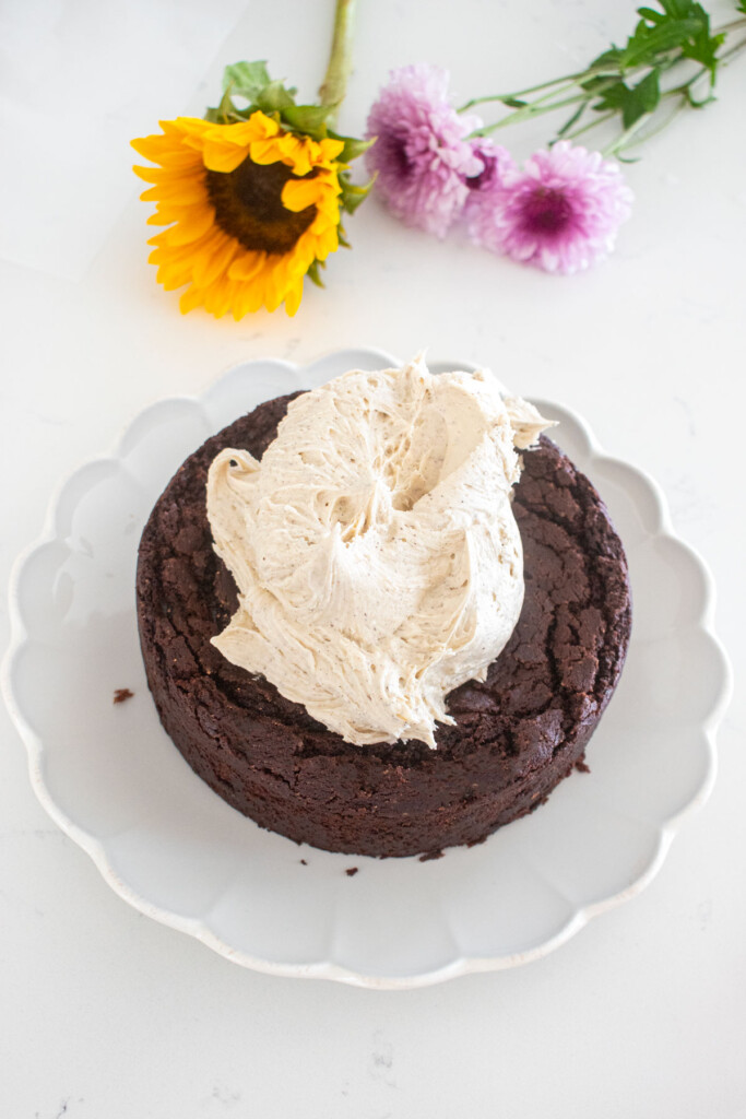 vegan sweet potato chocolate cake being assembled with vanilla frosting on a white marble counter.