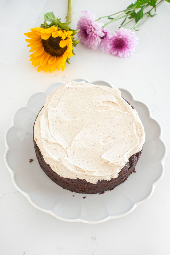 vegan sweet potato chocolate cake being assembled with vanilla frosting on a white marble counter.