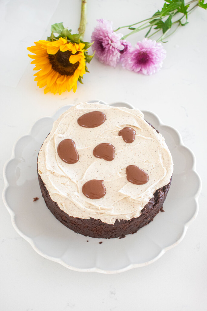 vegan sweet potato chocolate cake being assembled with vanilla frosting and chocolate ganache on a white marble counter.