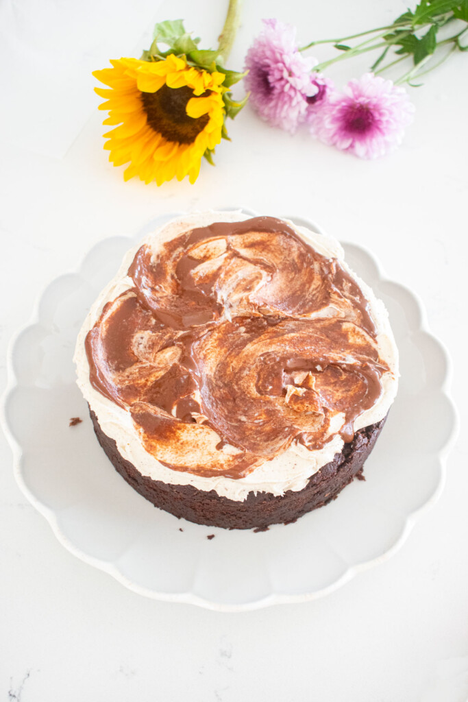 vegan sweet potato chocolate cake being assembled with vanilla frosting and chocolate ganache swirl on a white marble counter.