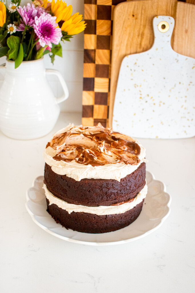 2 layer vegan sweet potato chocolate cake on a white ruffle plate on a marble counter with fresh flowers.