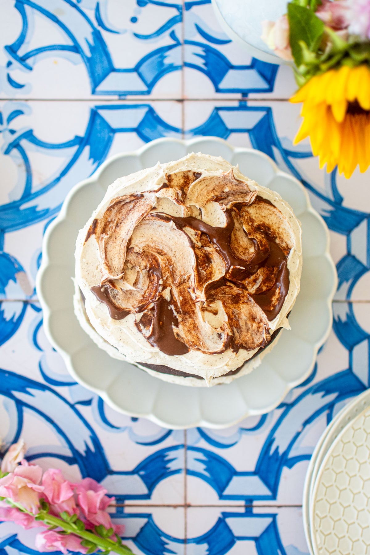 overhead of vegan sweet potato chocolate cake on a blue tile table with fresh flowers.