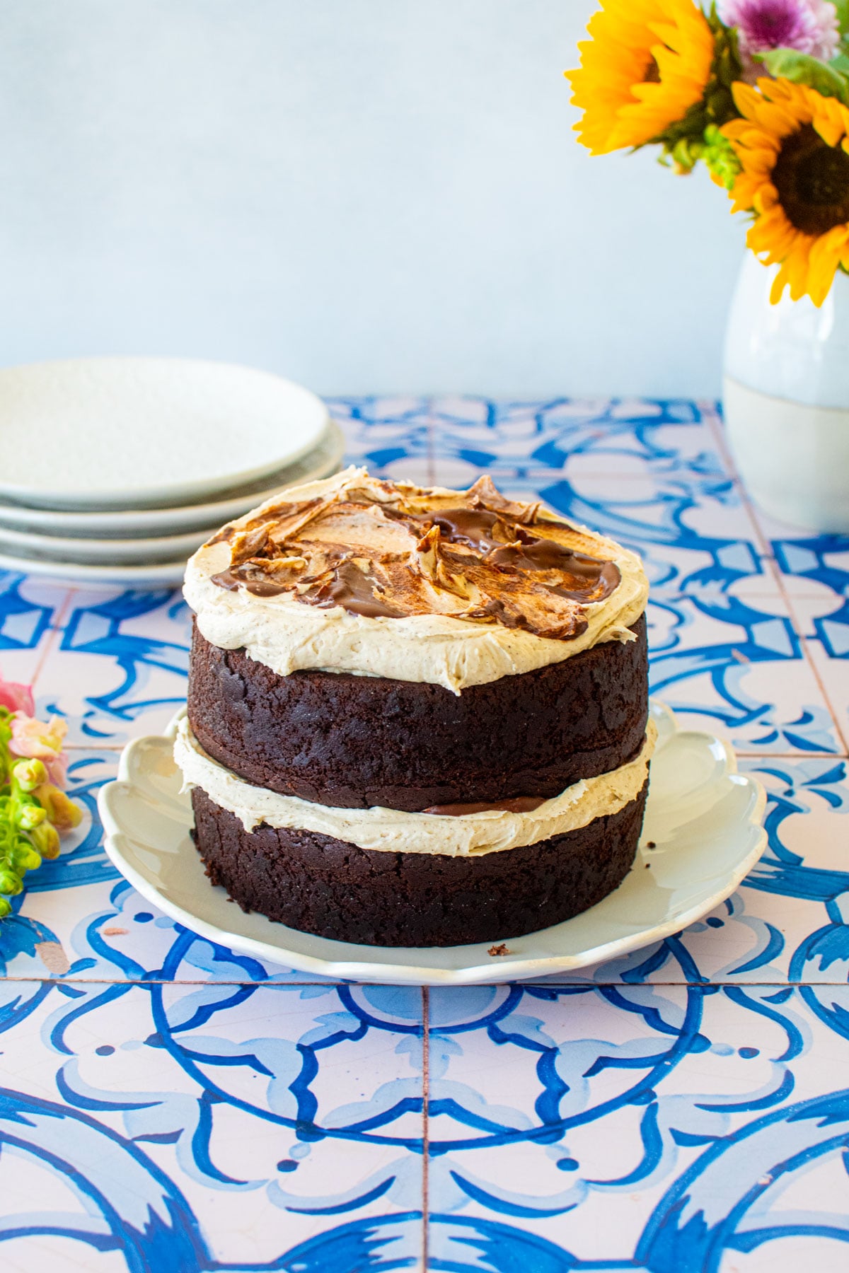 two layer vegan sweet potato chocolate naked cake on a blue tile table with fresh flowers.